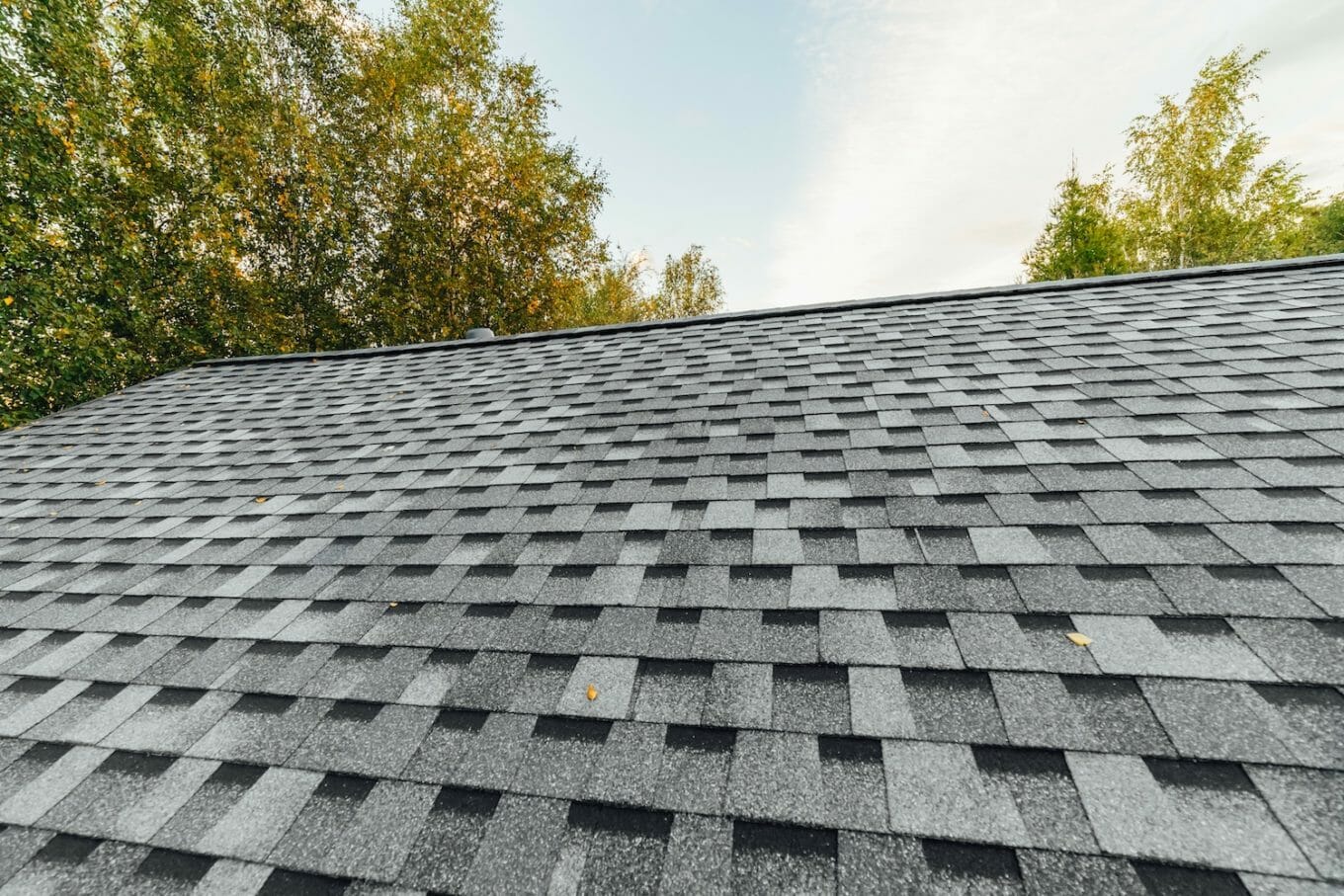 when to replace roof materials slanted view of asphalt shingle roof with sunny sky in background